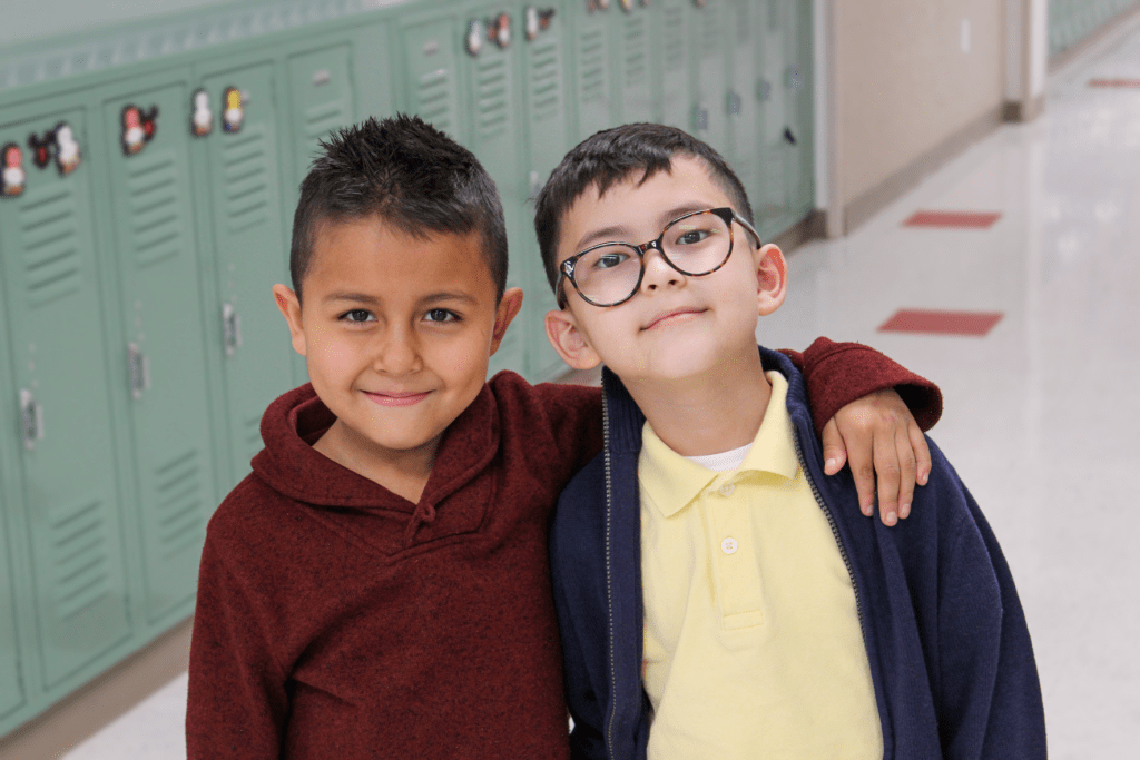 Two smiling male friends posing for a picture in the Guadalupe School hallway, one of them has their arm put around the shoulders of the other student.