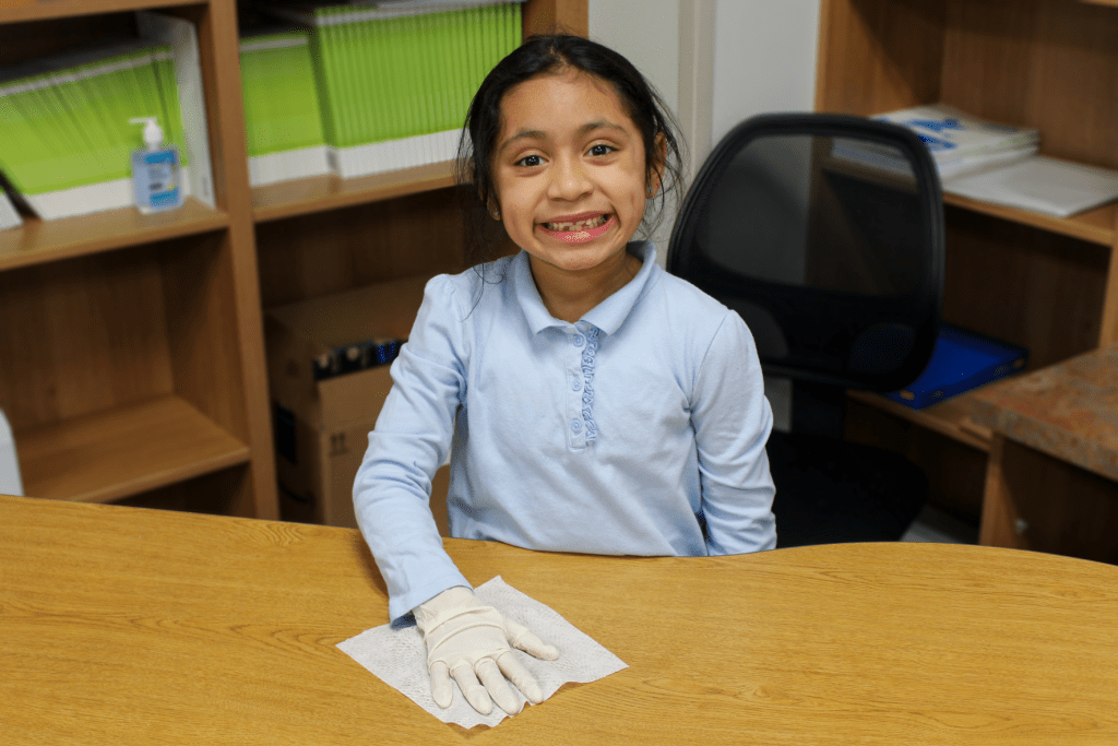 Guadalupe School student smiling and cleaning a classroom teacher's desk.