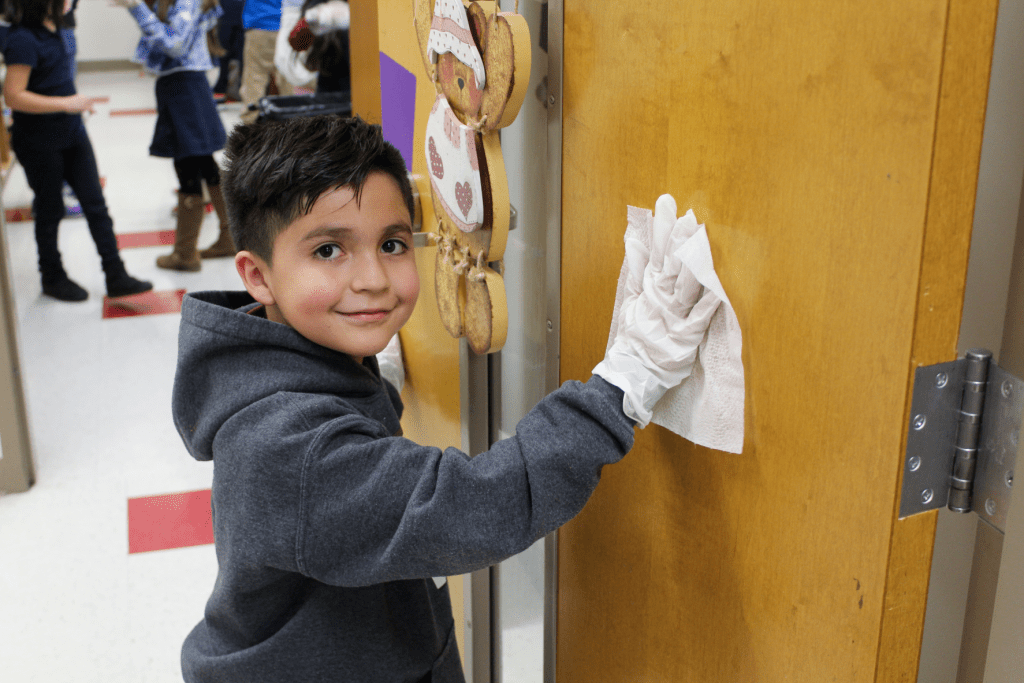 Guadalupe School student smiling and cleaning a classroom door.