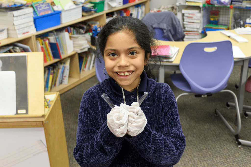 Guadalupe School student smiling and holding up garbage that she picked up while cleaning a classroom..
